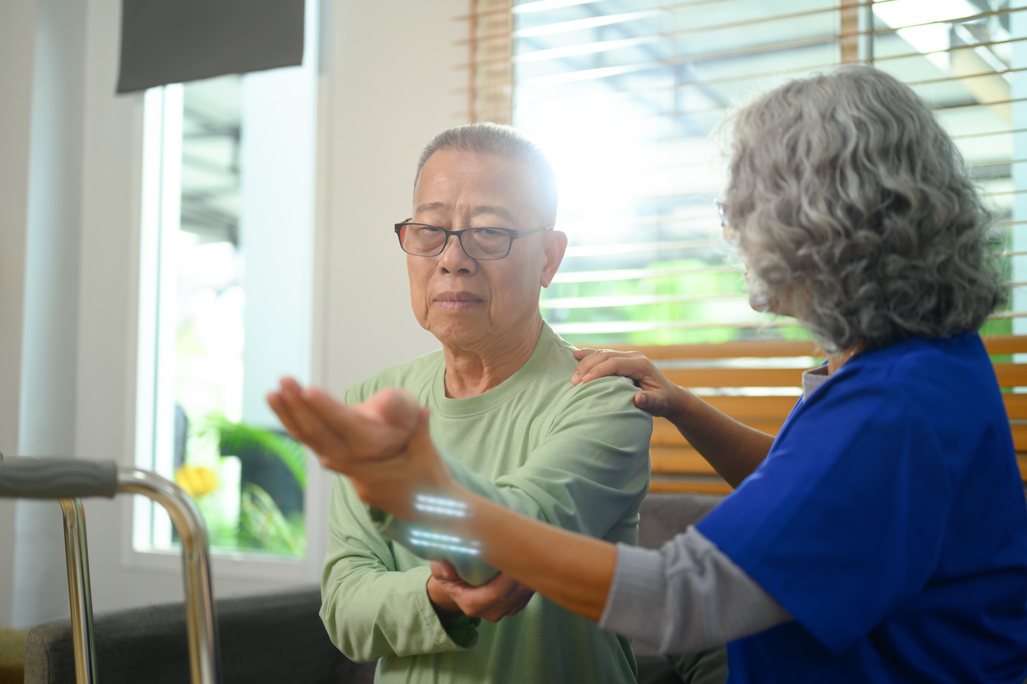 Elderly man exercising with his physiotherapist at home. Rehabilitation and healthcare concept